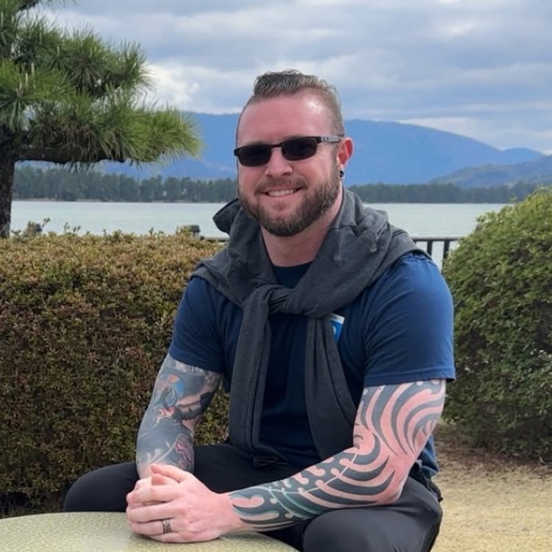 Dylan Priest, founder of 1UP Financial, smiling outdoors beside a lake